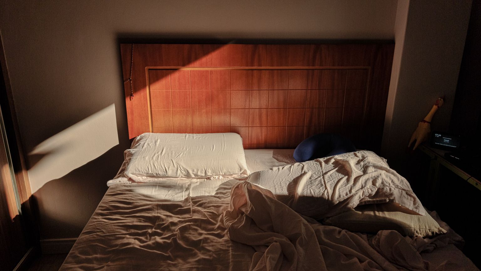 An unmade bed in low early morning sunlight