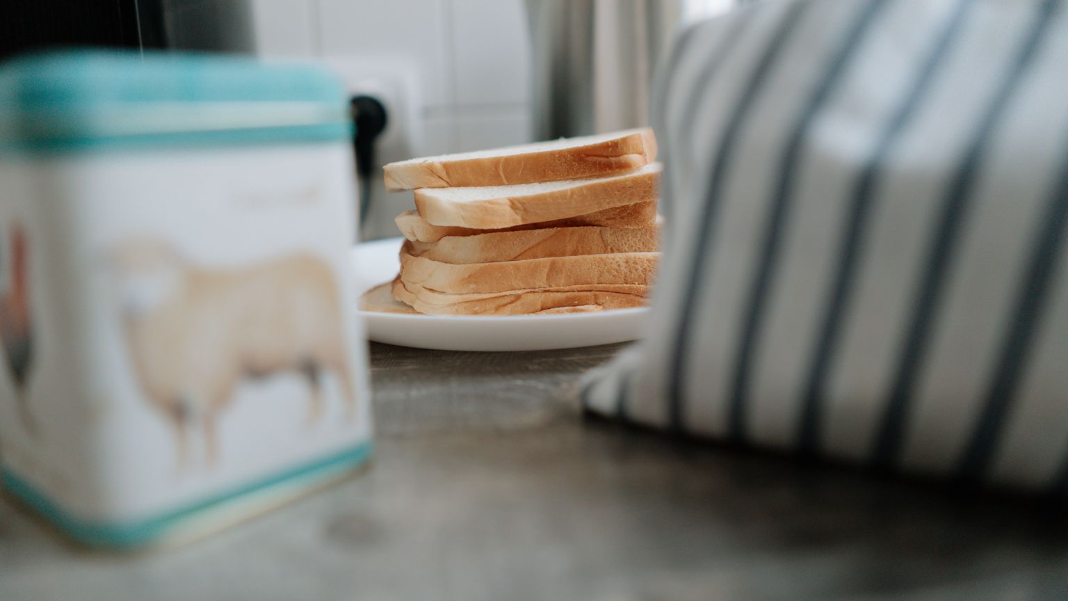 A stack of plain bread slices on a plate in a kitchen, untouched